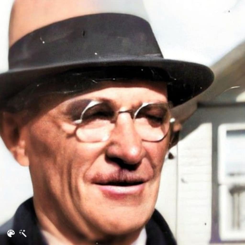 Headshot of a gentleman wearing glasses and a brown fedora