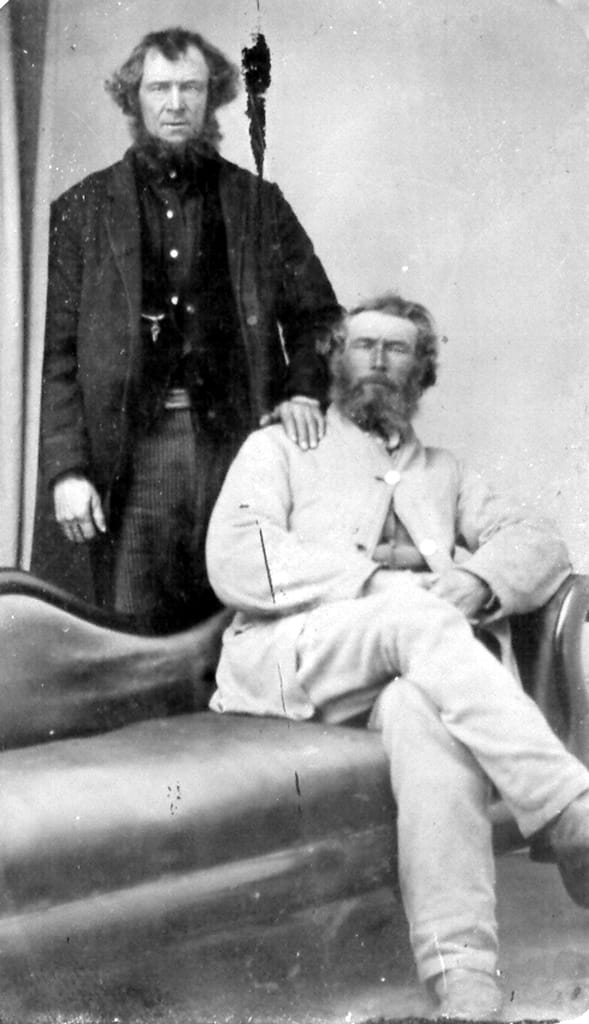 An ancient photograph of 2 middle aged men on sitting the other has his hand on the shoulder of the siting man.