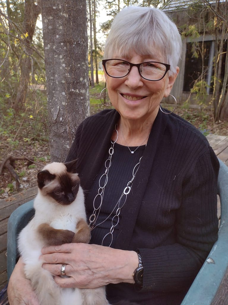 Woman smiling with a siamese cat on her knew.