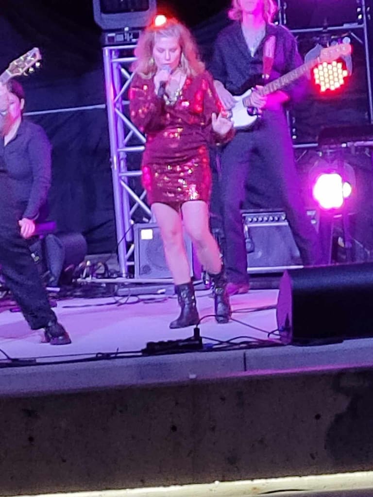 Young woman singing on a stage. she has a band behind her.