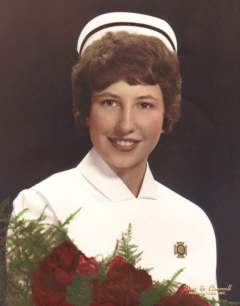 A women in a white uniform and a nurses cap with an armful of roses.