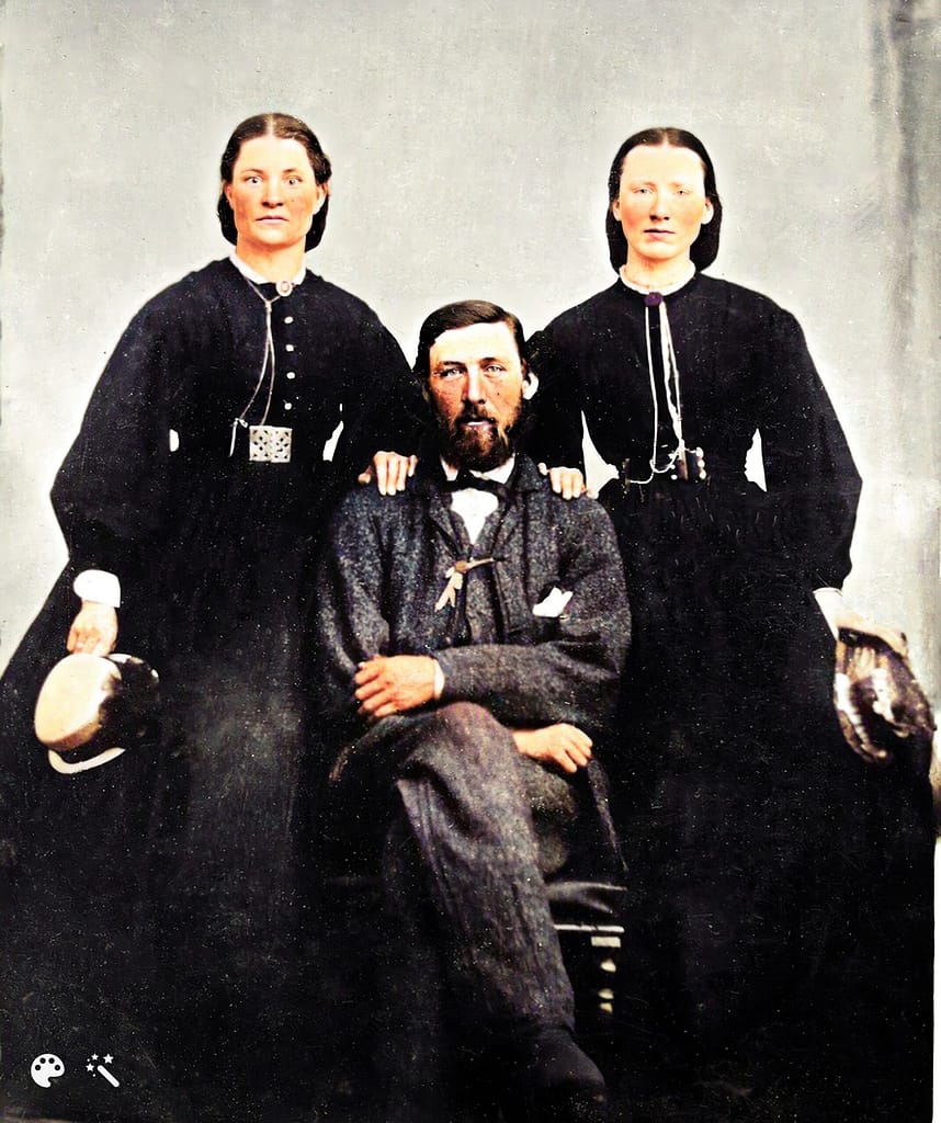 Two women standing with their hands on a sitting gentleman's shoulder