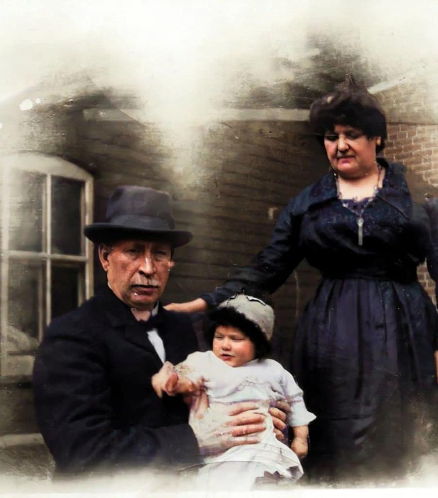 An older couple holding a baby. They are dressed in old fashioned clothes.