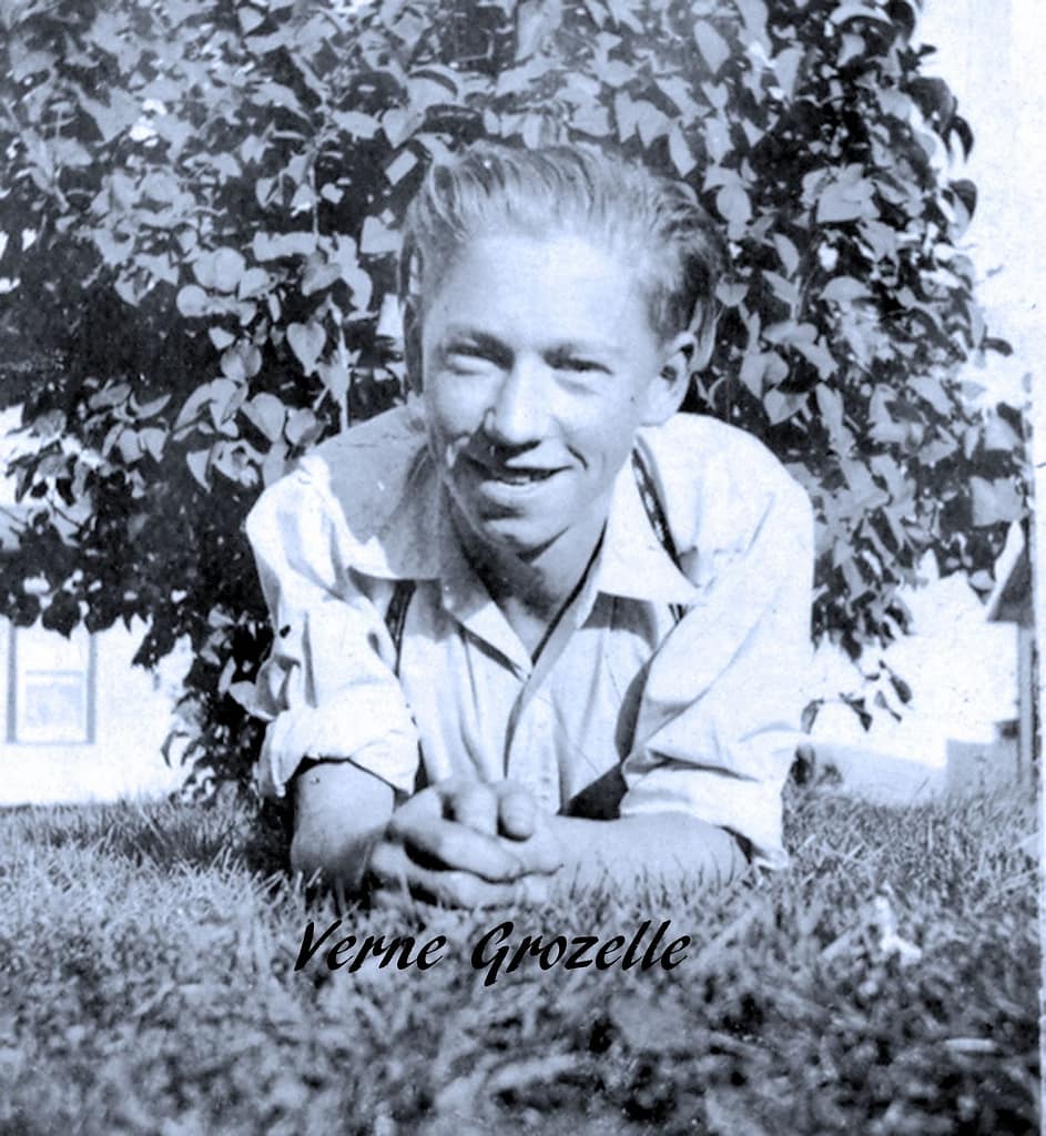 A young man lying on the grass under a tree facing the camera.