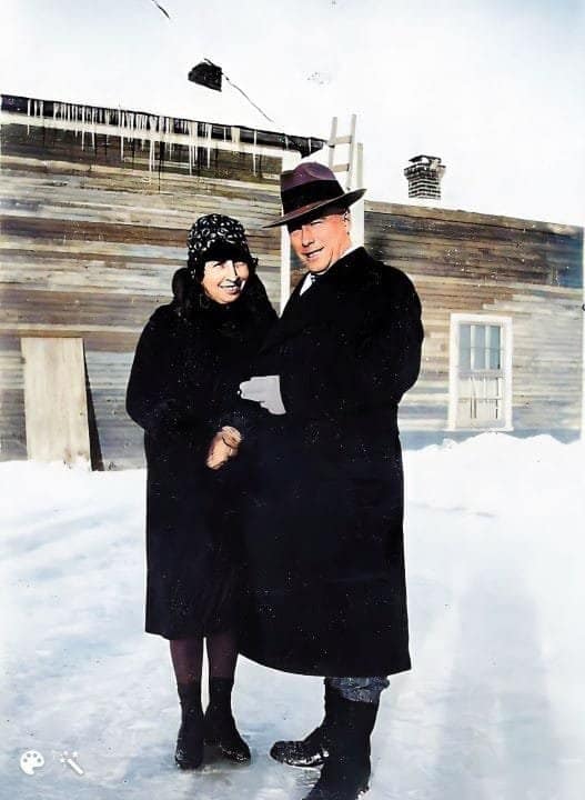 A man and woman posing outside dressed in black coats and hats.