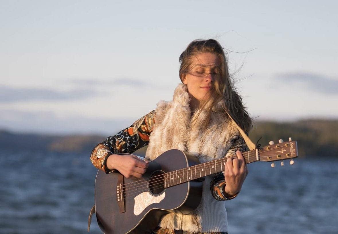 A young lady with a guitar. She is wearing a colourful outfit at the lagke.